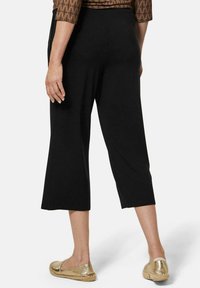 Zwarte cropped broek van zacht materiaal, met een wijd uitlopende pasvorm en een soepele tailleband. Gecombineerd met metallic gouden instappers.