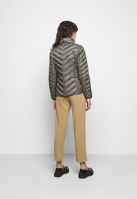 Veste en duvet matelassée avec un tissu à motif métallique, des coutures en chevron et un col montant, associée à un pantalon beige et des chaussures noires.
