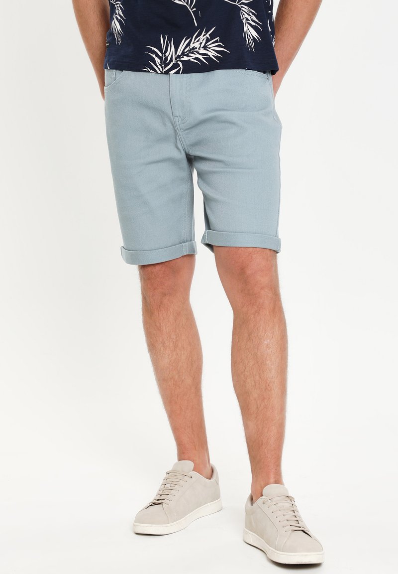 Pantalones cortos de color azul claro enrollados, hechos de tela de algodón, combinados con zapatillas beige. El diseño es simple con un ajuste casual.