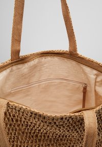 Vävd halm tote-väska med en beige tygfoder, med en dragkedjeficka, robusta vävda handtag och intrikat textur på utsidan.