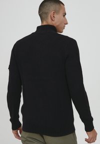 Schwarzer gestrickter Pullover mit hohem Kragen, gerippten Bündchen und Saum. Verfügt über ein strukturiertes Muster und eine figurbetonte Form.