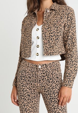 Kvinde iført matchende jakke og bukser i leopardmønster i brune og sorte nuancer med en hvid crop top med knapper under.
