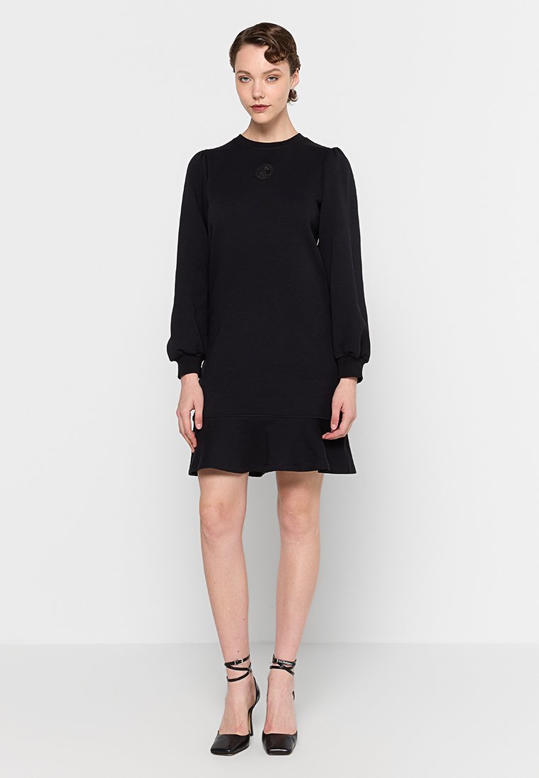 Robe noire avec de longues manches bouffantes et un ourlet évasé. Tissu doux et col rond. Petit logo accentué sur la poitrine.