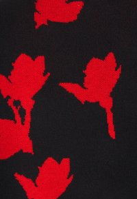 Gestrickter Pullover mit schwarzem Hintergrund und roten Blumenmustern. Die Textur ist glatt, und das Design umfasst verschiedene Blattformen.