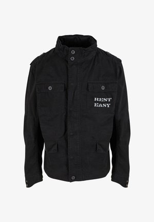 Musta takki, jossa on korkea kaulus, etunappikiinnitys, kaksi rintataskua ja vasemmassa rintataskussa painettu teksti "REST EASY".