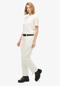 Camiseta de algodón blanca, combinada con pantalones rectos de color crema. Cinturón negro, botas de tobillo con cordones y un acabado brillante.