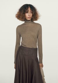 Maglione a maniche lunghe e collo alto in lana marrone chiaro, abbinato a una gonna plissettata marrone scuro, caratterizzata da una texture liscia e una silhouette aderente.