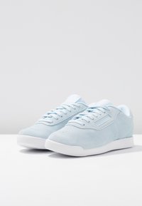 Baskets en daim bleu clair avec des semelles blanches, lacées, placées côte à côte sur une surface blanche devant un fond clair.