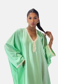 Kaftano verde in raso con maniche larghe, rifinitura ricamata color crema lungo lo scollo e i polsini, caratterizzato da un design ampio e fluente.