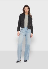 Giacca cropped in pelle nera con due cerniere frontali, abbinata a jeans a gamba larga blu chiaro e scarpe nere a punta. T-shirt grigia sotto.