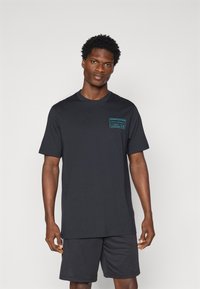 Zwarte katoenen t-shirt met korte mouwen, ronde hals, met een turkooizen grafische print op het linker borstgebied. Eenvoudig en recht gesneden ontwerp.