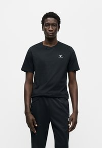 Μαύρο βαμβακερό t-shirt με στρογγυλή λαιμόκοψη, που φέρει ένα μικρό λευκό λογότυπο Converse στο στήθος. Φορεμένο με μαύρο αθλητικό παντελόνι.