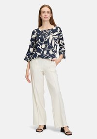 Navy top met bloemenprint, voorzien van een ronde halslijn en klokmouwen, gecombineerd met witte wijde broek en zwarte blockheel sandalen.