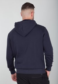 Felpa blu navy con cappuccio regolabile, maniche lunghe e polsini a costine. Tessuto morbido con una texture liscia, presenta una vita aderente. Senza loghi visibili.