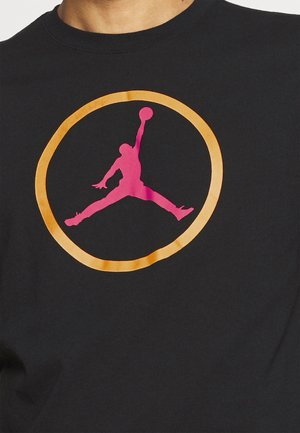 Black cotton t-shirt featuring a large, pink Jumpman logo inside an orange circle on the front, with a crew neck design.
