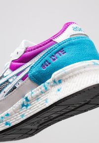 Sneaker featuring a white leather and mesh upper with turquoise and purple accents, textured midsole, and a patterned black rubber outsole.