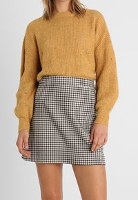 Musztardowy sweter dzianinowy z okrągłym dekoltem i długimi rękawami, zestawiony z czarno-białą mini spódniczką w kratę gingham o dopasowanym kroju.