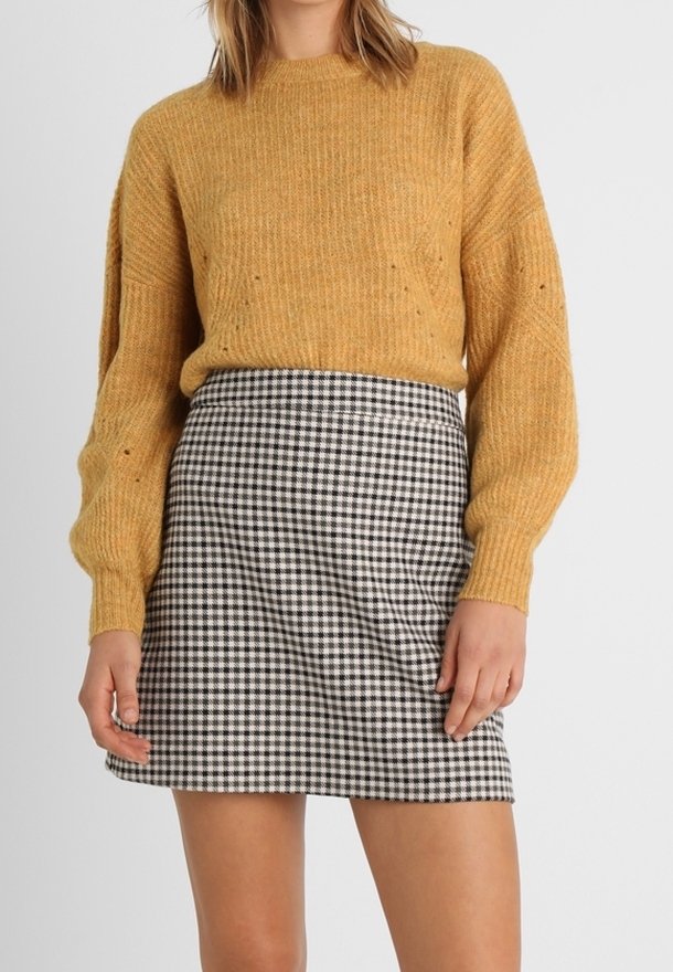 Musztardowy sweter dzianinowy z okrągłym dekoltem i długimi rękawami, zestawiony z czarno-białą mini spódniczką w kratę gingham o dopasowanym kroju.