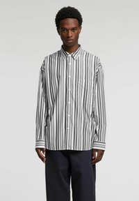 Koszula na guziki w paski w kolorze czarno-białym, z klasycznym kołnierzem, długimi rękawami i kieszenią na piersi. Bawełniana tkanina o gładkiej fakturze.