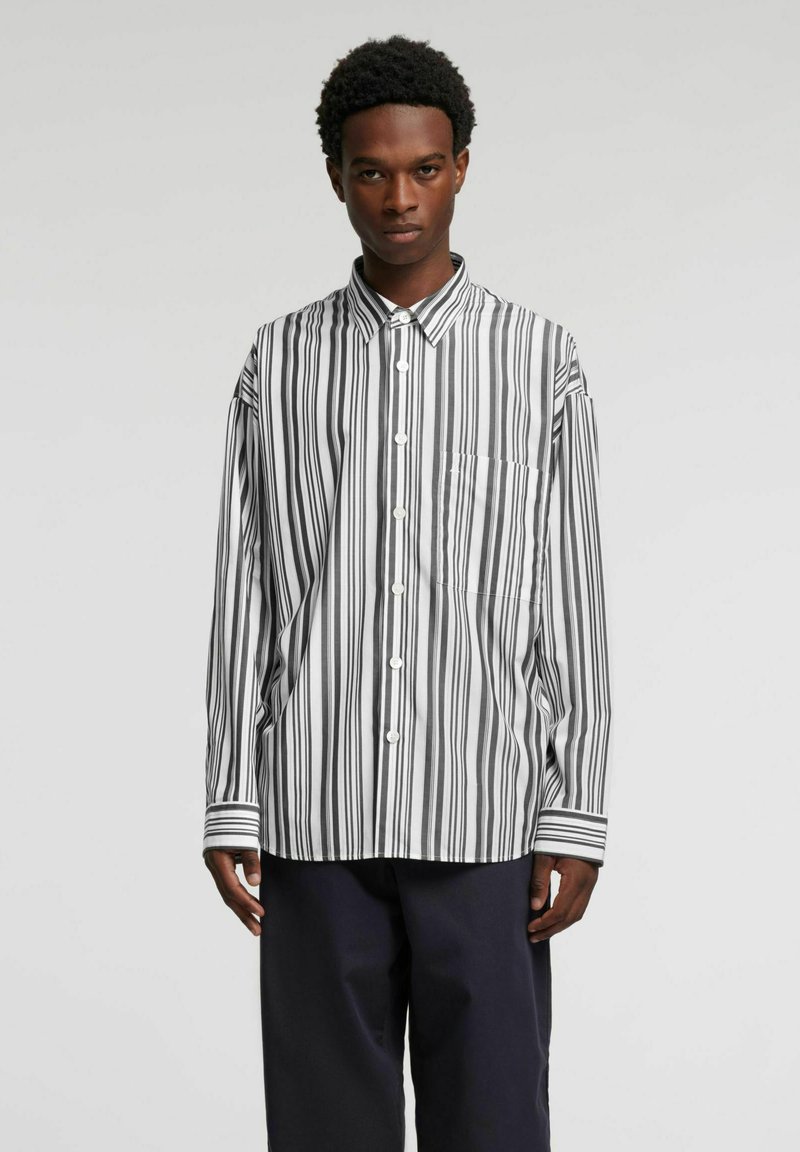 Koszula na guziki w paski w kolorze czarno-białym, z klasycznym kołnierzem, długimi rękawami i kieszenią na piersi. Bawełniana tkanina o gładkiej fakturze.