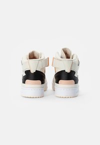 Mid-top sneakers i vitt och svart läder med en rosa mockadel. Har en vadderad krage och justerbar rem på hälen. Vit gummisula.