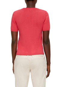 Kortärmad, figurnära korallfärgad stickad tröja med rund halsringning och ribbade detaljer i kanterna. Enfärgad textur och sömlig rygg.