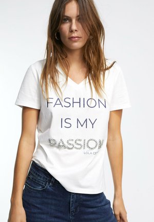 Camiseta de algodón blanca con cuello en V que presenta el texto "LA MODA ES MI PASIÓN" en color navy, adornada con cristalitos en la palabra "PASIÓN."