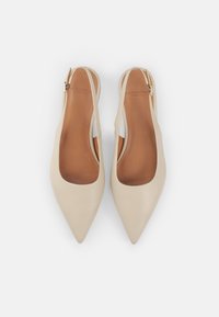 Zapatos slingback de punta afilada en color beige, hechos de cuero suave, presentan un tacón bajo y una hebilla lateral para ajustabilidad, con una plantilla en tono marrón.