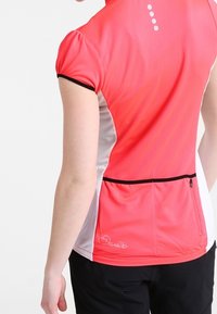 Koszulka sportowa z krótkim rękawem w gradientowym różu, z szarymi akcentami. Posiada kieszeń z tyłu na suwak oraz małe dekoracyjne białe kropki na linii dekoltu.