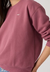 Φούτερ Levi's σε ξεθωριασμένο ροζ, κατασκευασμένο από απαλό ύφασμα, με ριμπ μανσέτες, στρογγυλή λαιμόκοψη και μικρό λογότυπο στο στήθος.