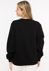 Schwarzer übergroßer Sweatshirt mit Rundhalsausschnitt, überschnittenen Schultern und gerippten Bündchen. Weicher Stoff mit glatter Oberfläche. Schlichtes Design, keine Muster.