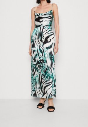 Vrouw draagt een mouwloze, enkellange jurk met een abstract dierenprint in zwart, wit en teal, gecombineerd met zwarte gevlochten open-toe hakken.