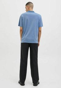 Šviesiai mėlynas medvilnės mišinio polo marškinėliai trumpomis rankovėmis su klasikinio stiliaus apykakle. Dėvimi su laisvai krentančiomis juodomis kelnėmis ir juodais batais.