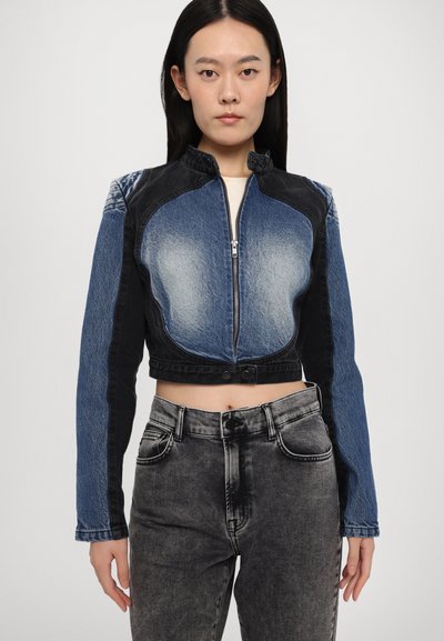 Cropped denim jacket with a mix of dark and light blue fabrics. Design features a high collar and a front zipper. Paired with black denim jeans.