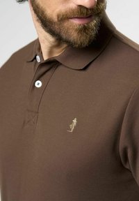 Braunes Poloshirt aus strukturiertem Stoff, mit einer Dreiknopf-Leiste und einem in Gold gestickten Logo auf der linken Brust.