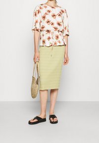 Kwiatowy top peplum w pomarańczowe maki, zestawiony z prążkowaną, jasnobrązową spódnicą midi. W zestawie pleciona torebka i czarne klapki dopełniają look.