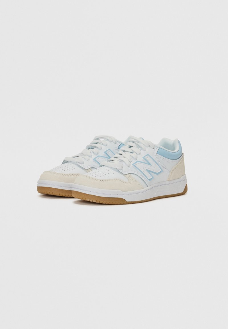 Zapatillas blancas y azul claro hechas de cuero y ante, con puntera perforada, cordones blancos y suela de goma. Logo de New Balance en el lateral.