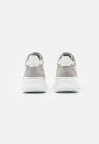 Paire de baskets en daim gris avec semelles blanches épaisses, vues de dos sur un fond blanc.