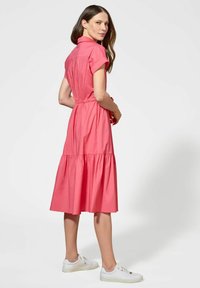 Różowa bawełniana sukienka z krótkimi, zakręconymi rękawami, kołnierzykiem i warstwową spódnicą. Szczegóły obejmują elastyczny pas i zapięcie na guziki z tyłu.