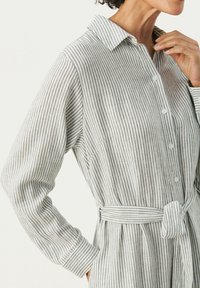 Abito a righe bianco e grigio, realizzato in un tessuto dalla consistenza morbida. Presenta un colletto, bottoni e un dettaglio in vita legato. Maniche lunghe.
