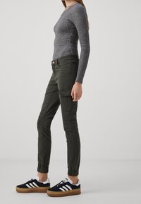 Top de manga larga gris claro con textura acanalada, combinado con pantalones cargo verde oliva que cuentan con bolsillos laterales y puños elásticos, acompañado de zapatillas negras y blancas.