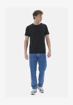 Mustat puuvillapaita, jossa on pyöreä kaula-aukko, yhdistettynä sinisiin farkkuihin. Mallilla on päällään harmaat lenkkarit. Yksinkertainen ja rento muotoilu.