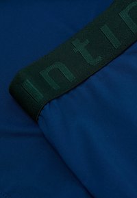 Modrá atletická látka s hladkým povrchem, vybavená tmavě zeleným elastickým páskem s vyraženým nápisem podél horního okraje.