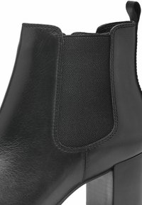 Black ankle boot featuring a leather upper, elastic side panels, and a block heel. Smooth texture with stitched detailing and a sleek silhouette.