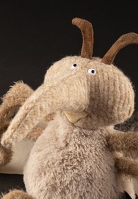 Soft, plush toy with a long, textured, beige snout, brown antennae, and large round eyes, featuring fuzzy fur and a round body.