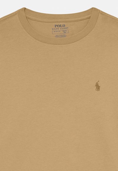 Μπεζ βαμβακερό μπλουζάκι με στρογγυλή λαιμόκοψη, διακοσμημένο με ένα μικρό λογότυπο κεντημένο σε σκούρο νήμα στην αριστερή πλευρά του στήθους. Μαλακή υφή, κοντά μανίκια.