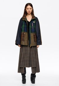 Barvna plaid jakna z zelenimi, modrimi in rjavimi poudarki; ima zadrgo in gumbne zap closures, velike žepe; v kombinaciji z dolgo plaid krilo.