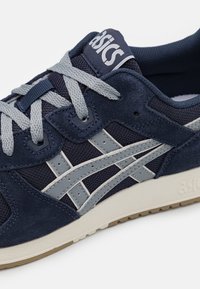 Mornarsko modra športna obuvala iz usnja in mreže, s sivo vezalkami, Asicsov logo na ježku in kremasto obarvan gumijast podplat.