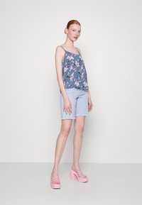 Top sin mangas floral en azul, combinado con pantalones cortos de mezclilla claros. Zapatos de plataforma gruesos en rosa con detalles trenzados. Diseño simple, estilo casual.