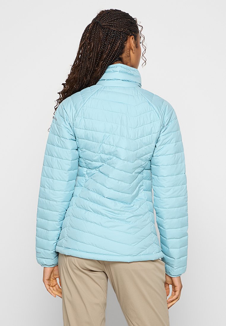 Chaqueta acolchada de color azul claro con cuello alto y puños acanalados, que presenta patrones de costura en diagonal y una silueta ajustada.